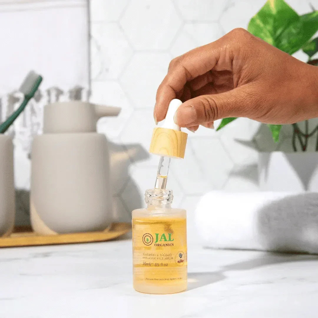 Hand holding a dropper over a Jal Organics skincare serum bottle, part of the 5-Piece Blueberry Rhubarb Skin Care Set.