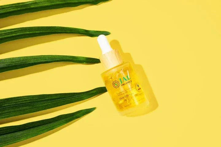 Yellow bottle of Jal Organics serum on a yellow background with green leaves, part of the 5-Piece Blueberry Rhubarb Skin Care Set.
