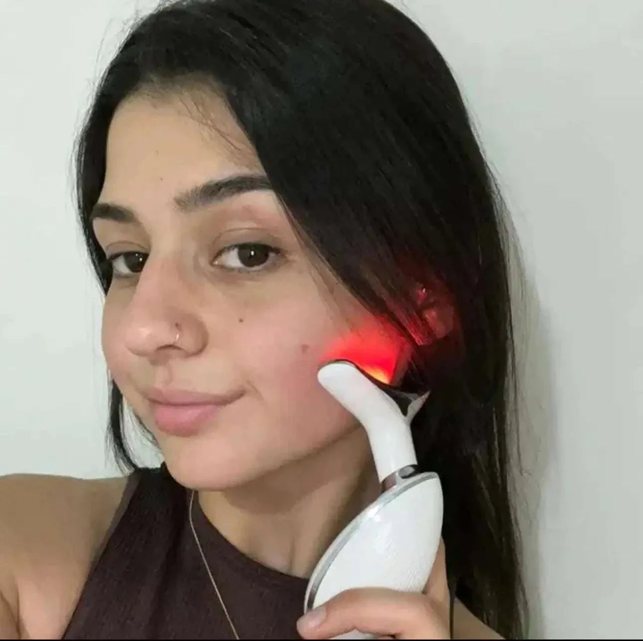 Woman using beauty device with red light on cheek for anti-wrinkle treatment