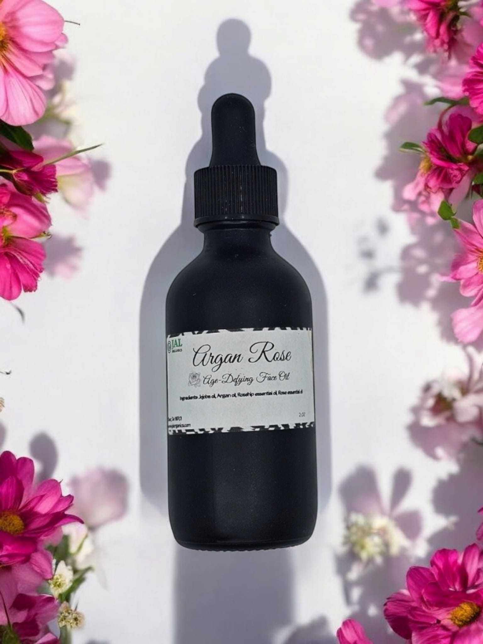 Argan Rose Face Oil Serum bottle surrounded by pink flowers.