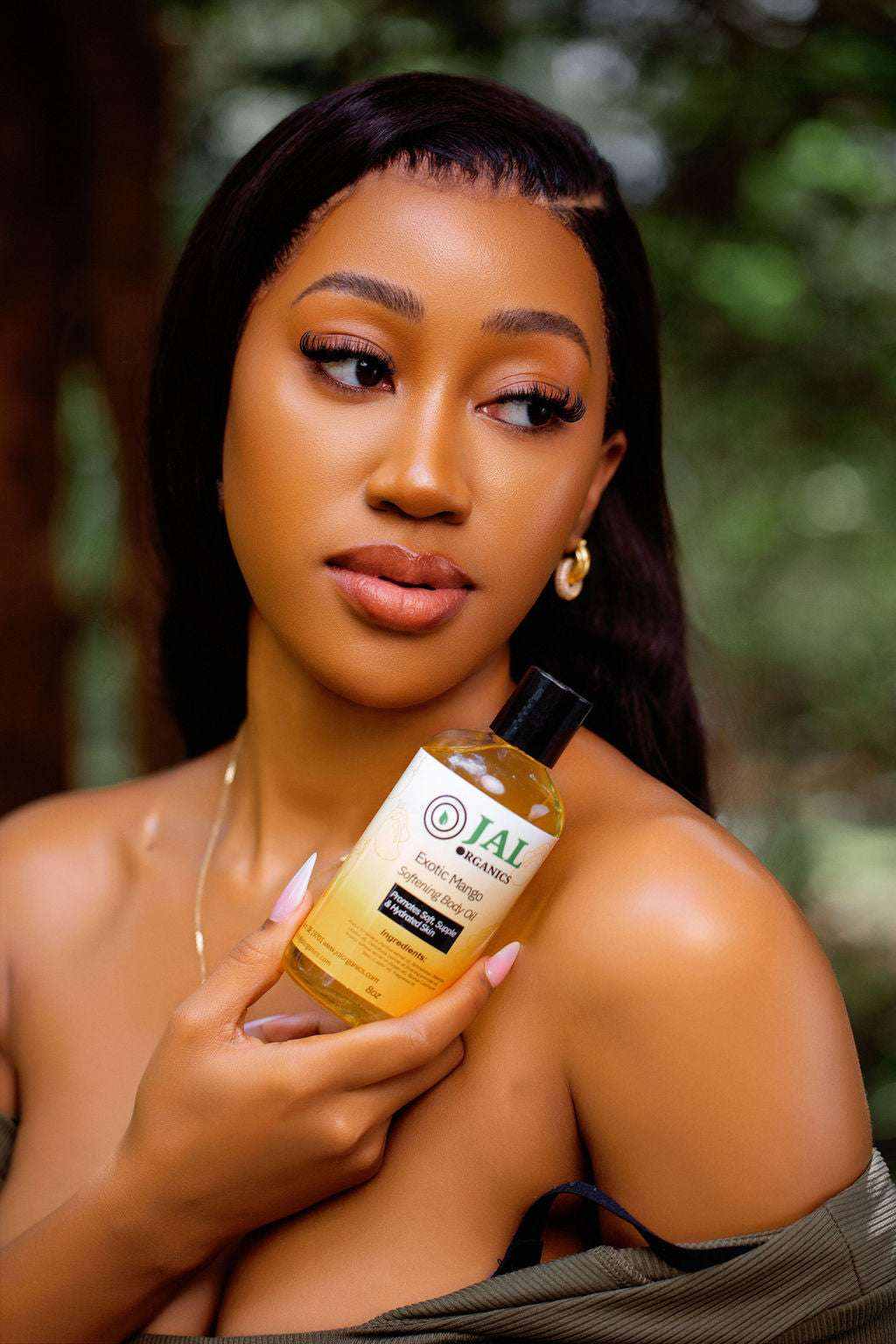 Exotic Mango Body Oil held by woman with glowing skin and elegant earrings.