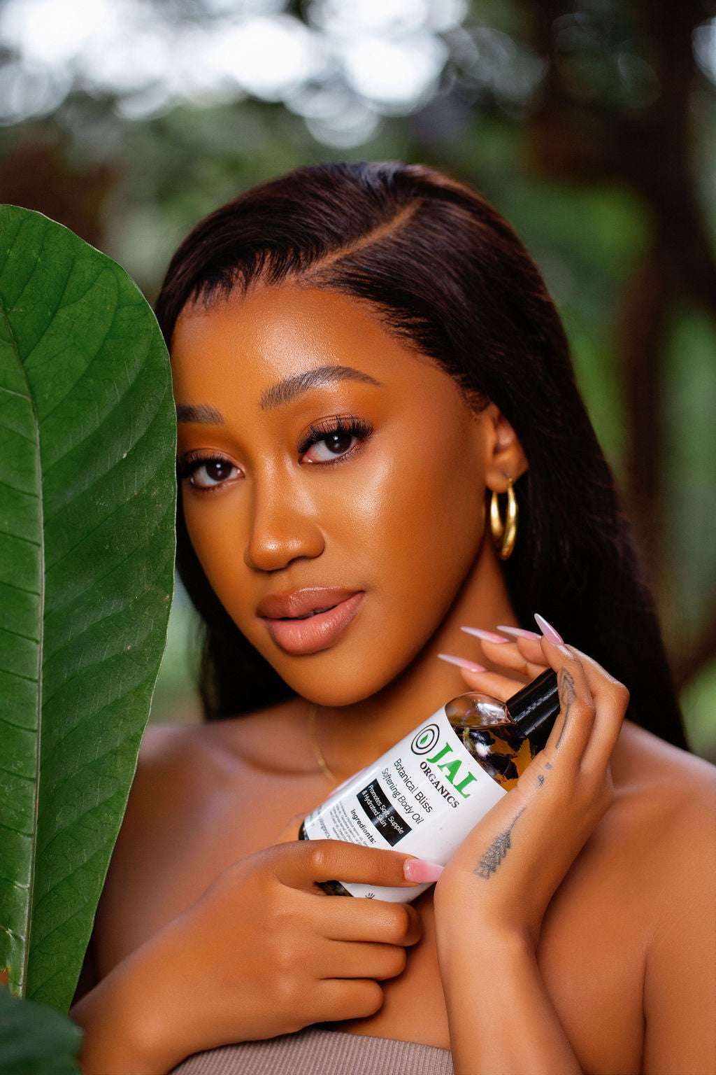 Botanical Bliss Body Oil held by a model against a lush green background.