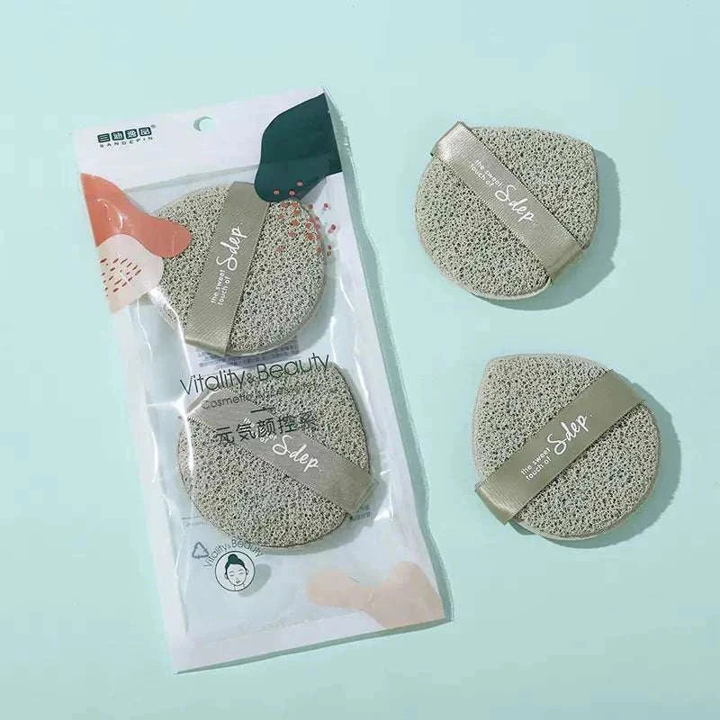 Travel-ready exfoliating face puff set with two round, gray polyurethane puffs in clear packaging on light blue background