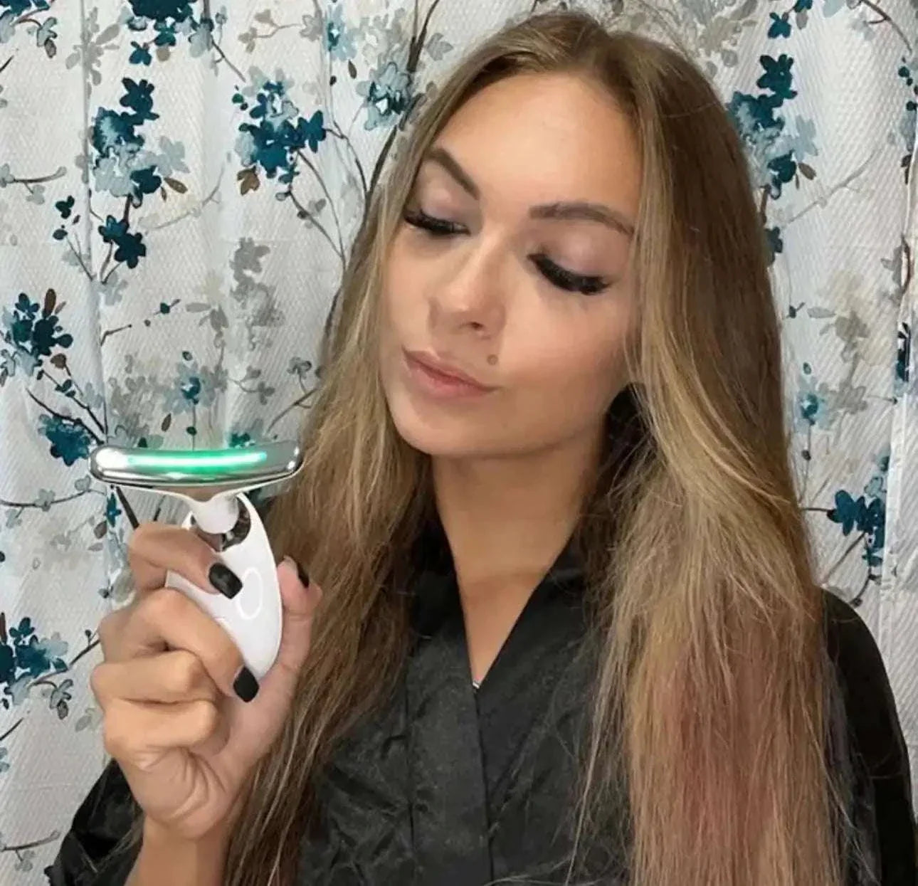 Woman using anti-wrinkle beauty device with green light on face against floral background
